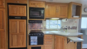 A kitchen with wooden cabinets, a microwave, a stove, and a window.