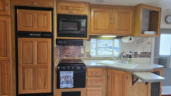 A kitchen with wooden cabinets, a microwave, a stove, and a window. - Bunker Hill Hideaway Ramble RV Suite (Kingston)