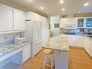 A kitchen with white cabinets, a granite countertop, a refrigerator, and a bar stool. - Family-Friendly Corvallis Home Near OSU & Parks (Corvallis)