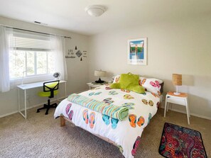 Ein Schlafzimmer mit Bett, Schreibtisch, Stuhl, Nachttisch, Lampe, einem Fenster mit Vorhängen und einem Poster an der Wand.