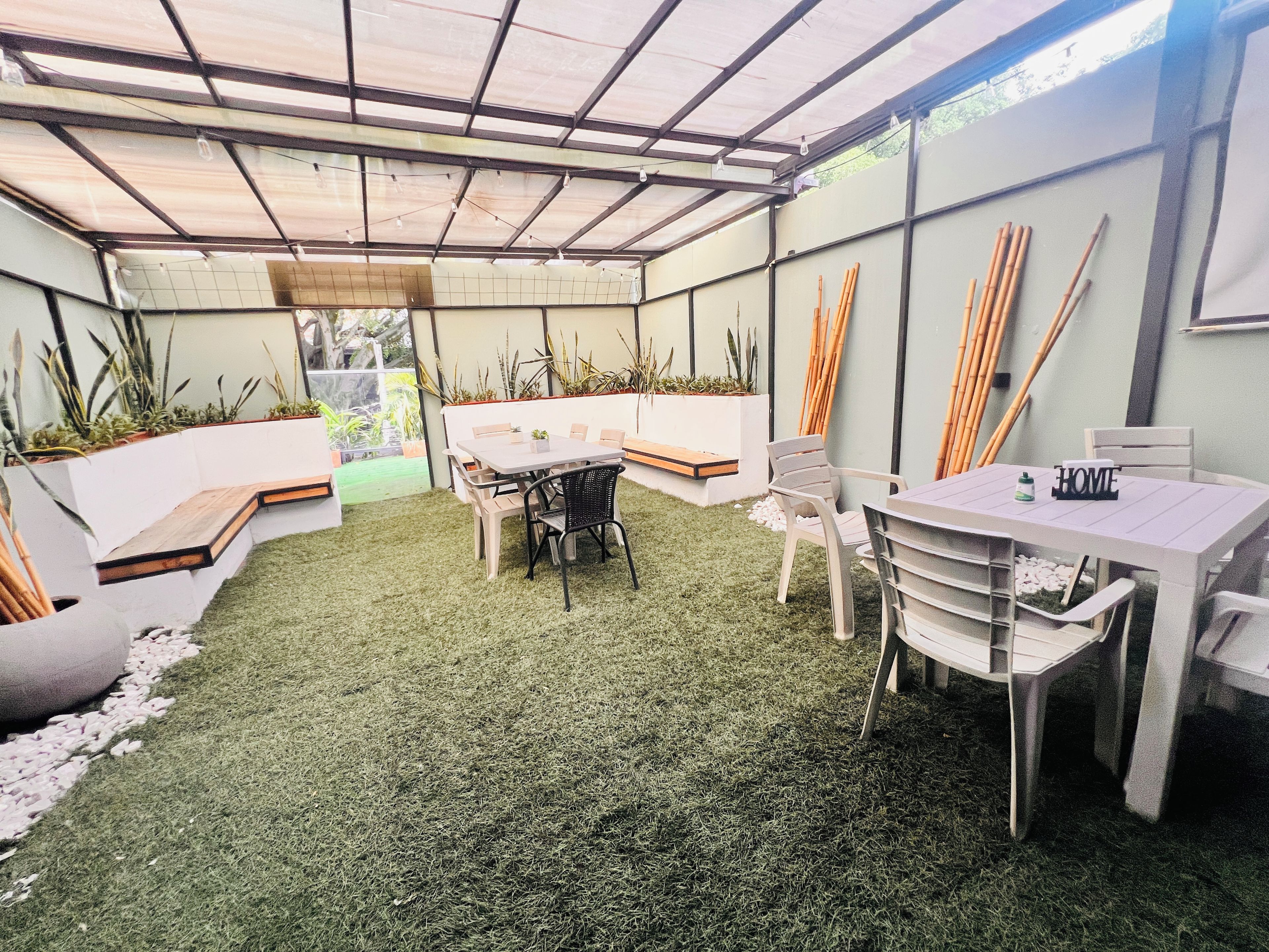 A covered patio area with a table and chairs, surrounded by planters and a grassy floor.