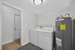 Ein Waschraum mit Waschmaschine und Trockner, einer Tür und einem an der Wand montierten Warmwasserbereiter.