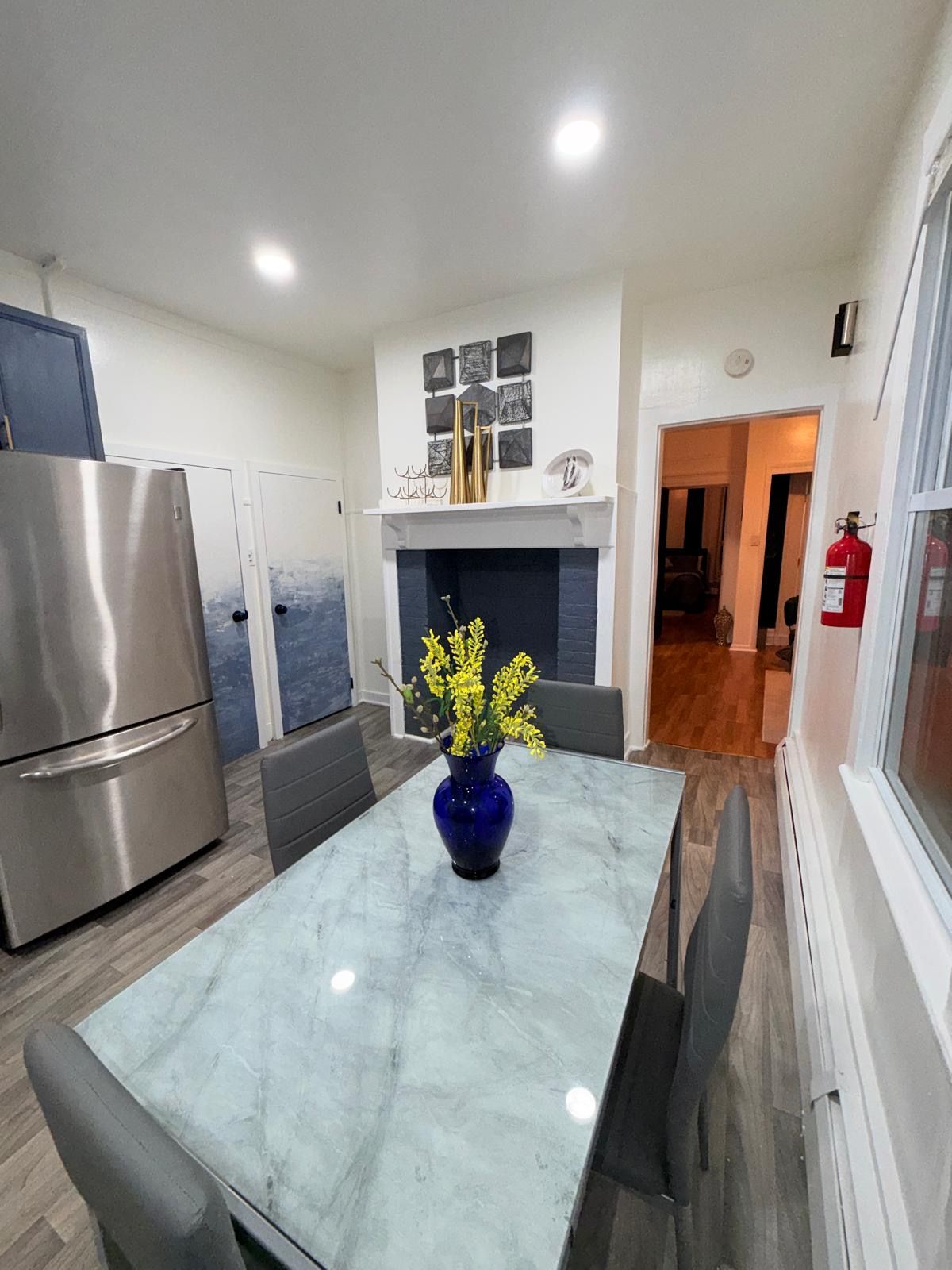 A modern kitchen with a marble table, a stainless steel refrigerator, and a blue vase with yellow flowers.