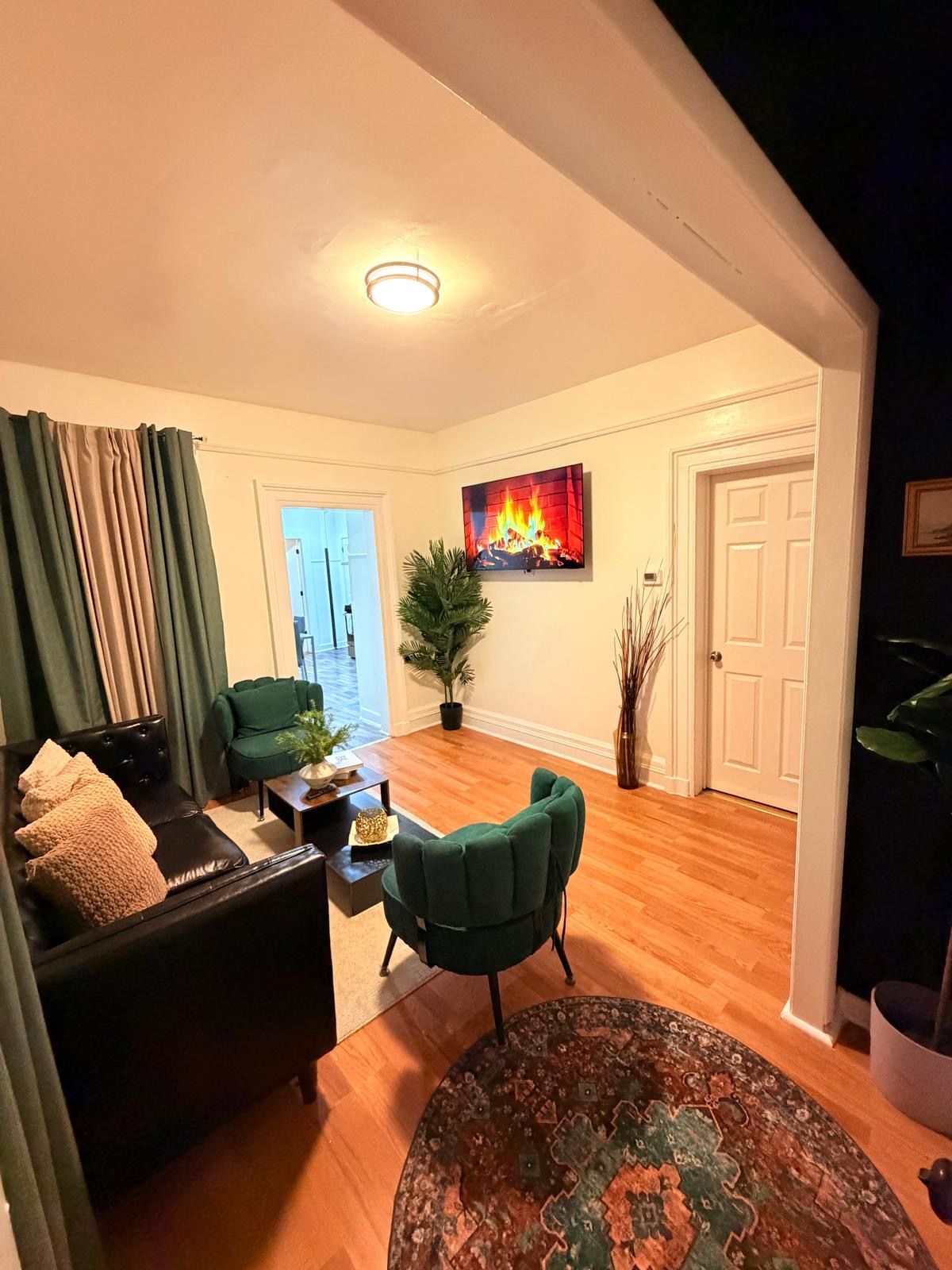 A living room with a sofa, a green armchair, a coffee table, and a rug. There is a painting of a fire on the wall.