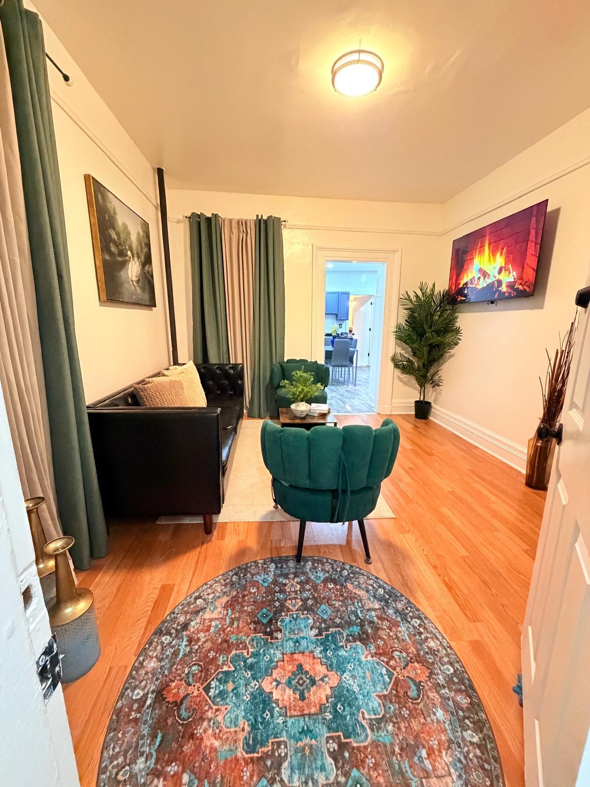 A living room with a sofa, a green armchair, a patterned rug, and a painting of a fire.