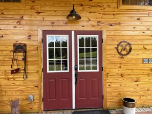 A wooden cabin with a red double door, a small porch light, and a metal bucket. - Delightful 1-Bedroom Barn Apartment Located In Gated Equestrian Community (Aiken)