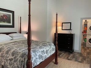 A four-poster bed with a patterned bedspread, a dark wooden dresser, a framed map, and a laundry area with a washing machine. - Delightful 1-Bedroom Barn Apartment Located In Gated Equestrian Community (Aiken)
