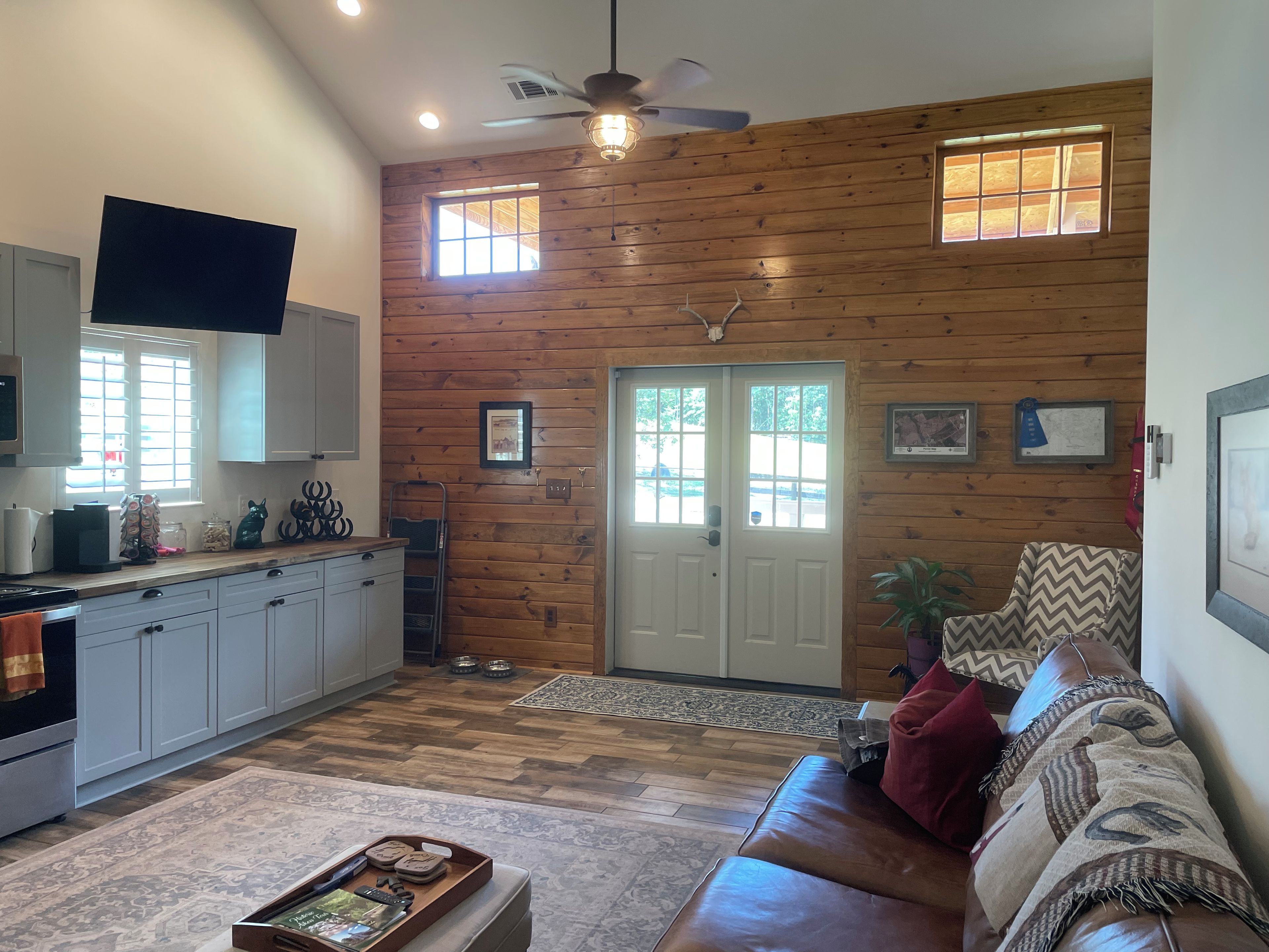 A spacious living area with a wooden wall, a ceiling fan, a television, and a sofa.