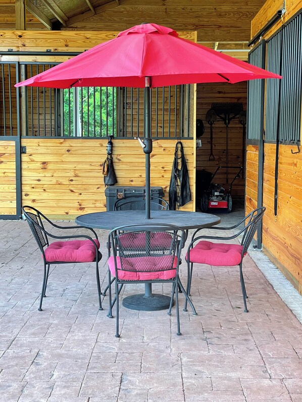 Uma cabana de madeira com uma mesa redonda e duas cadeiras, um guarda-chuva vermelho e um portão de metal.