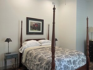 Een hemelbed met een bloemenbedekker, een ingelijste foto aan de muur en twee bedlampen.