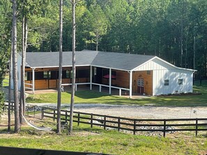 A two-story building with a covered riding area and a fenced yard. - Delightful 1-Bedroom Barn Apartment Located In Gated Equestrian Community (Aiken)