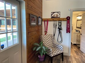 A room with a wooden wall, a window, a chair, a potted plant, and a wall-mounted rack with items. - Delightful 1-Bedroom Barn Apartment Located In Gated Equestrian Community (Aiken)