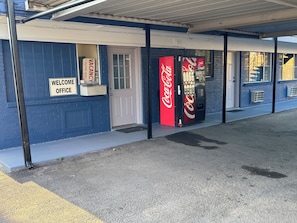 A building with a 'Welcome Office' sign, a Coca-Cola vending machine, and a door.
