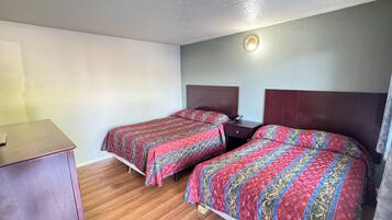 A room with two beds, a wooden floor, a desk, and a wall-mounted light fixture.