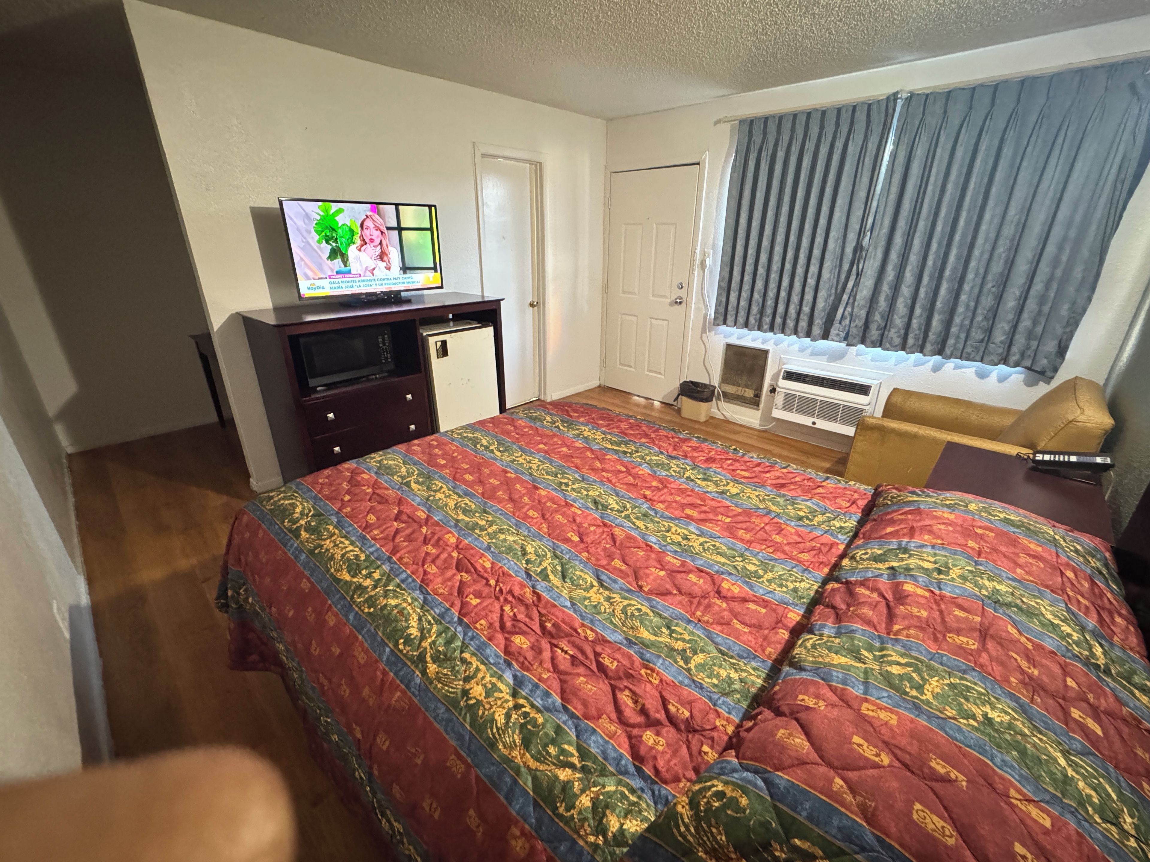 Una habitación de hotel con cama, televisión, escritorio, silla y ventana con cortinas.