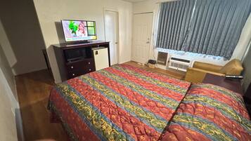 Una habitación de hotel con cama, televisión, escritorio, silla y ventana con cortinas.