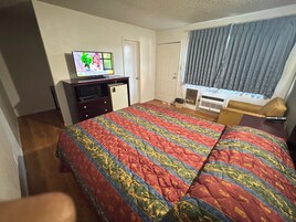 A hotel room with a bed, a television, a desk, a chair, and a window with curtains.