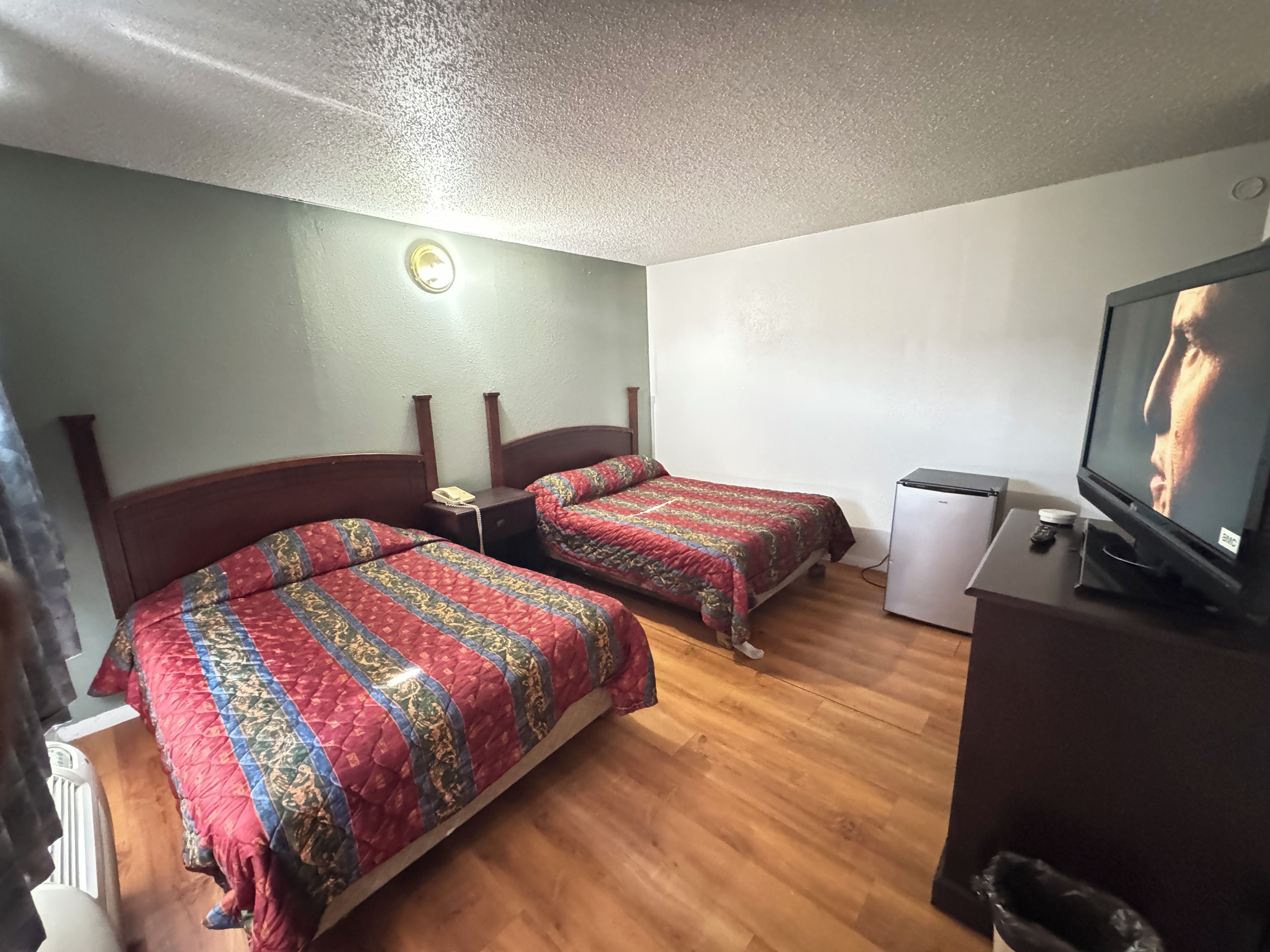 Habitación de hotel con dos camas, un refrigerador pequeño, un televisor y una mesita de noche con teléfono.