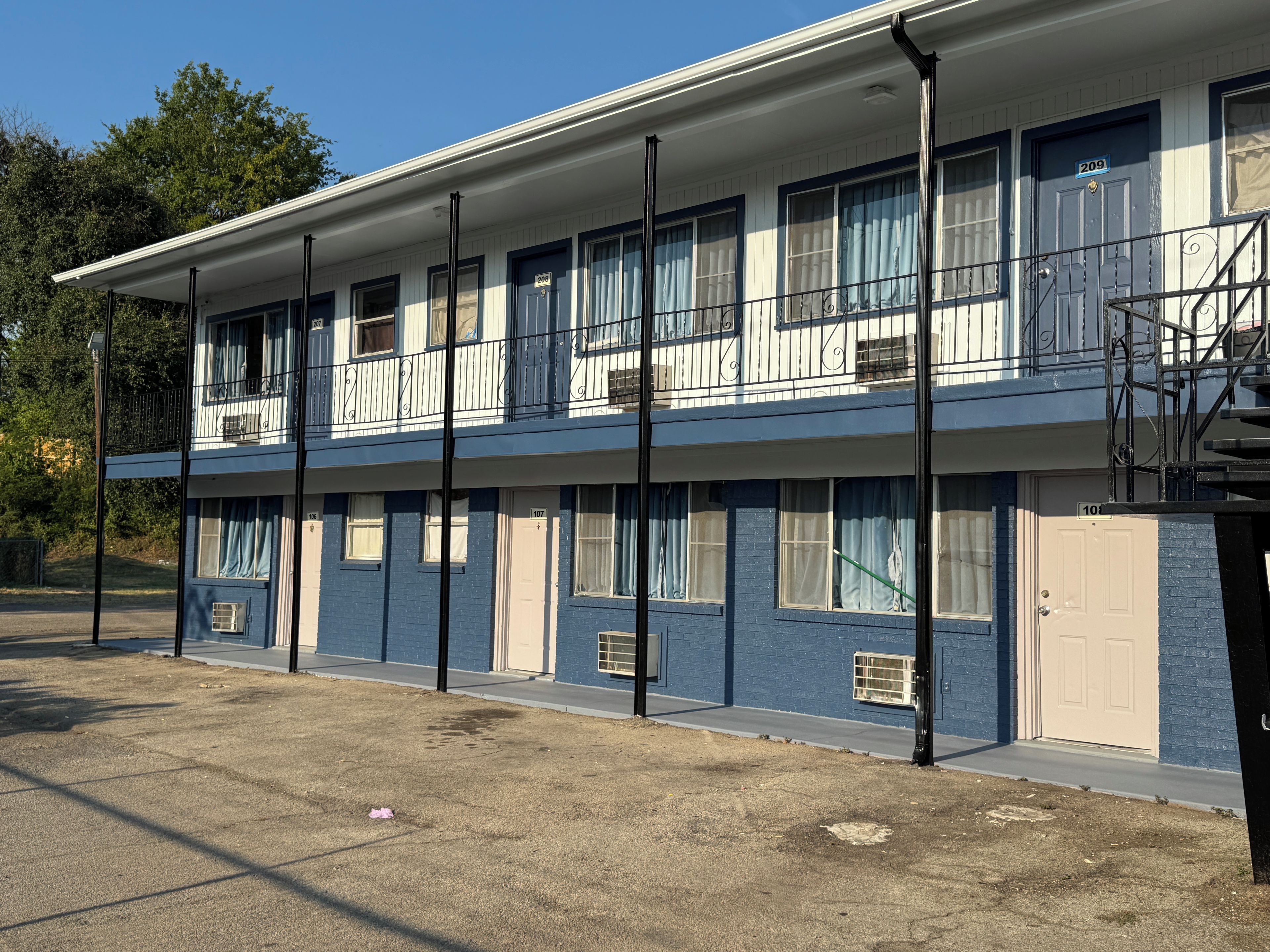 Ett motell i två våningar med en enkel fasad, numrerade dörrar och en balkong på övervåningen.