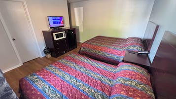 A bedroom with two beds, a TV on a dresser, a microwave, and a small cabinet.