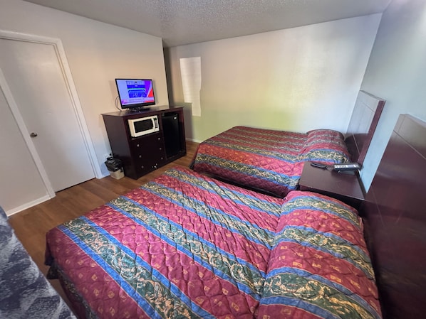 A bedroom with two beds, a TV on a dresser, a microwave, and a small cabinet.