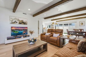A modern living room with a leather sofa, a coffee table, a TV, and artwork on the walls. - LongBeach LaVerne Beauty - Monthly Rental By Water (Long Beach)