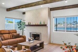A living room with a leather sofa, a fireplace, a coffee table, and a view of the sea through a window with a black railing. - LongBeach LaVerne Beauty - Monthly Rental By Water (Long Beach)