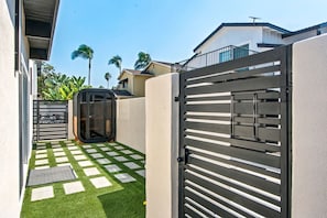A gated entrance with a checkered pathway leading to a covered area, surrounded by a modern building with a balcony. - LongBeach LaVerne Beauty - Monthly Rental By Water (Long Beach)