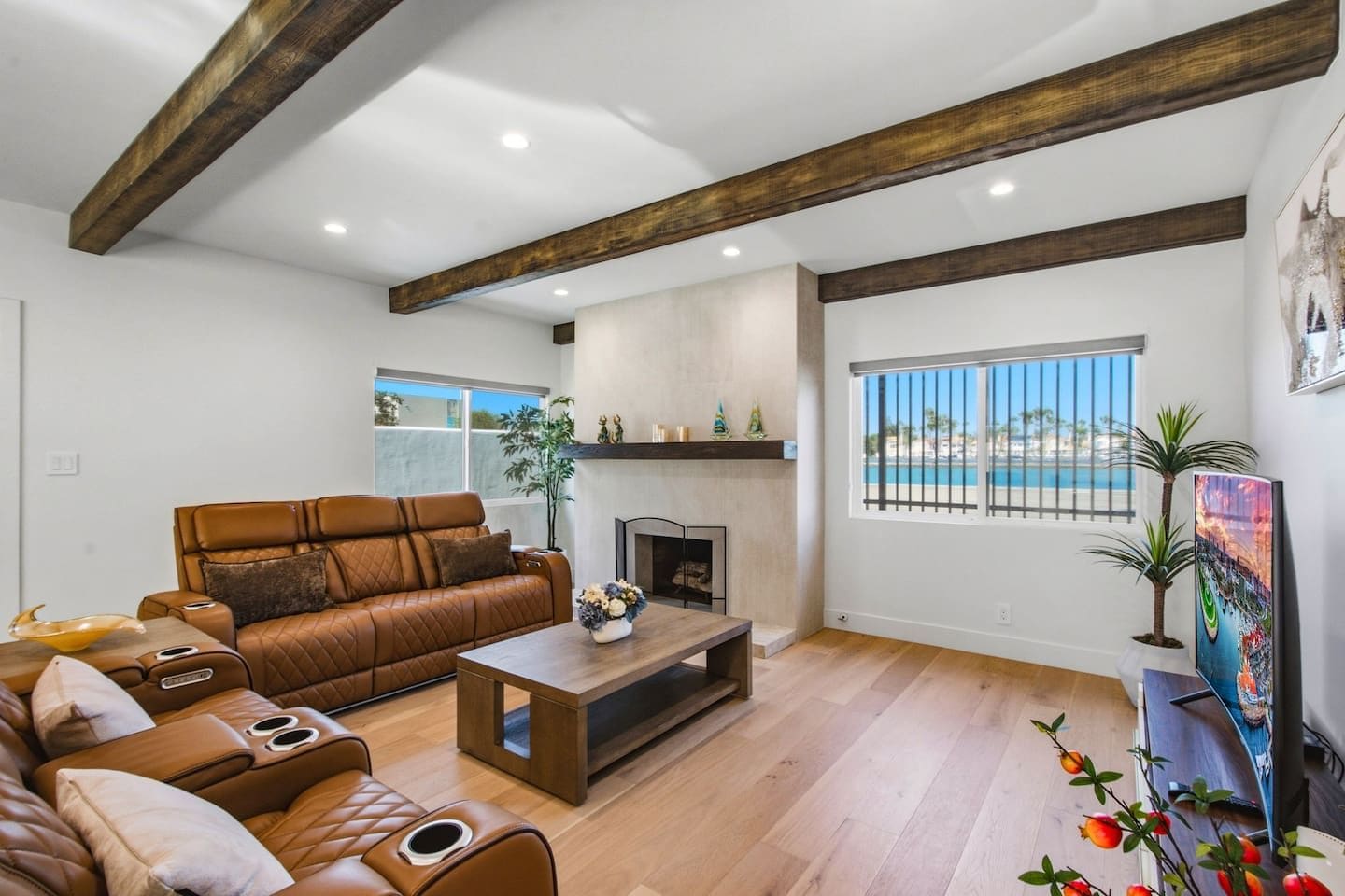 A modern living room with a leather sofa, a fireplace, wooden flooring, and a large window with a view.