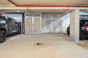 A parking garage with two cars parked, a concrete floor, and a metal gate with a mesh design. - Coastal Outlook - Caloundra Poolside Apartment (Caloundra Region)