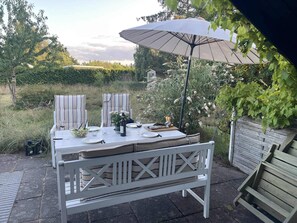 Eine Terrassengruppe im Freien mit Tisch für zwei Personen, einer Bank und Sonnenschirm.