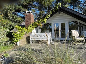 Ein Haus mit Schornstein aus Backstein, einer weißen Veranda und einer Glastür, die auf eine überdachte Terrasse führt.