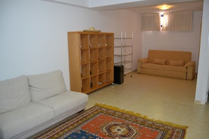 A living room with a sofa, a wooden bookshelf, a small table, and a patterned rug. - Bahía Meloneras Villas Bahmel01 (San Bartolomé de Tirajana)