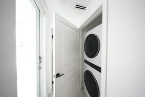 A laundry room with two stacked washing machines, a white door, and a ceiling vent. - Luxury Pool Villa (Palmetto Bay)