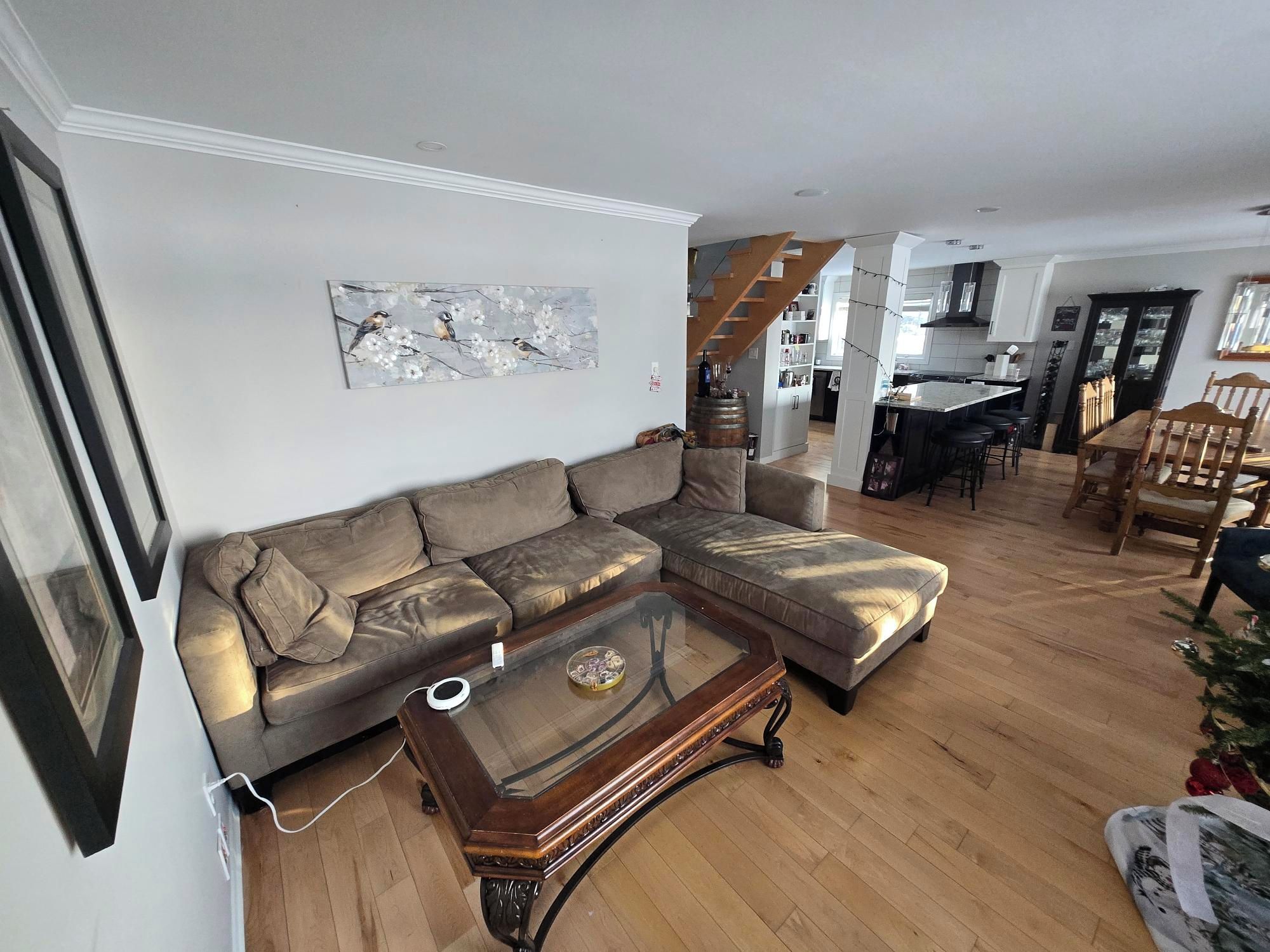 Ein Wohnzimmer mit einem Ecksofa, einem Glastisch und einem Bild an der Wand.
