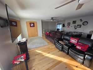 A living room with a leather sofa, a flat-screen TV, and a ceiling fan.