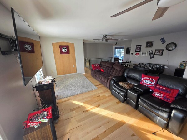 A living room with a leather sofa, a flat-screen TV, and a ceiling fan.