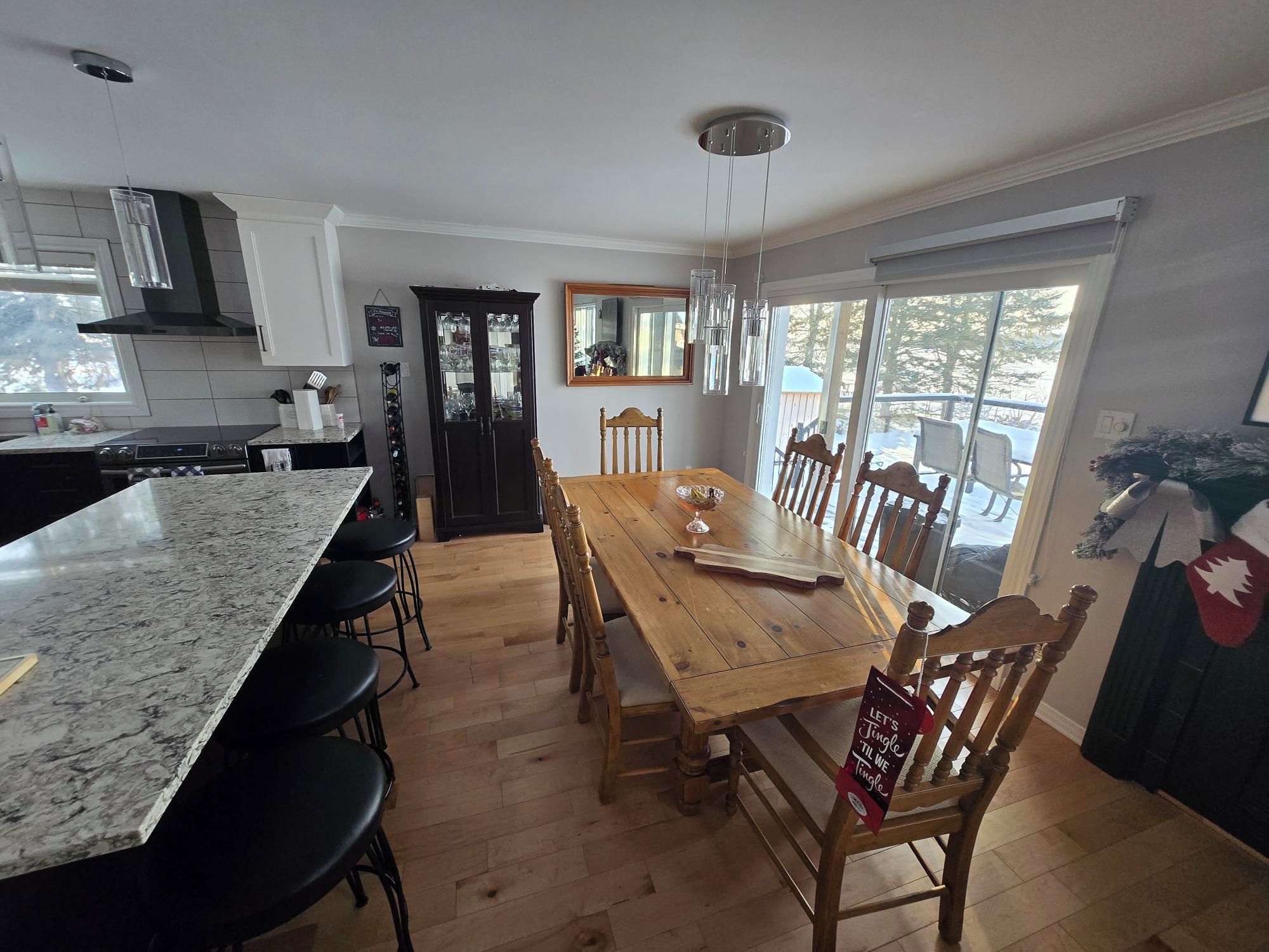 Een keuken met een groot eiland, een houten eettafel en stoelen. Er is een raam met uitzicht op bomen.