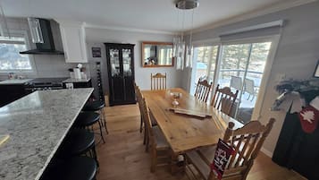 Een keuken met een groot eiland, een houten eettafel en stoelen. Er is een raam met uitzicht op bomen.
