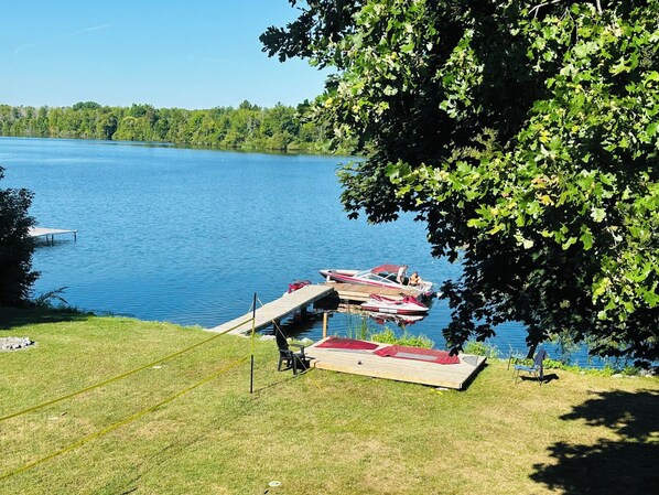 A lakeside dock with boats, a grassy area, and a tree.