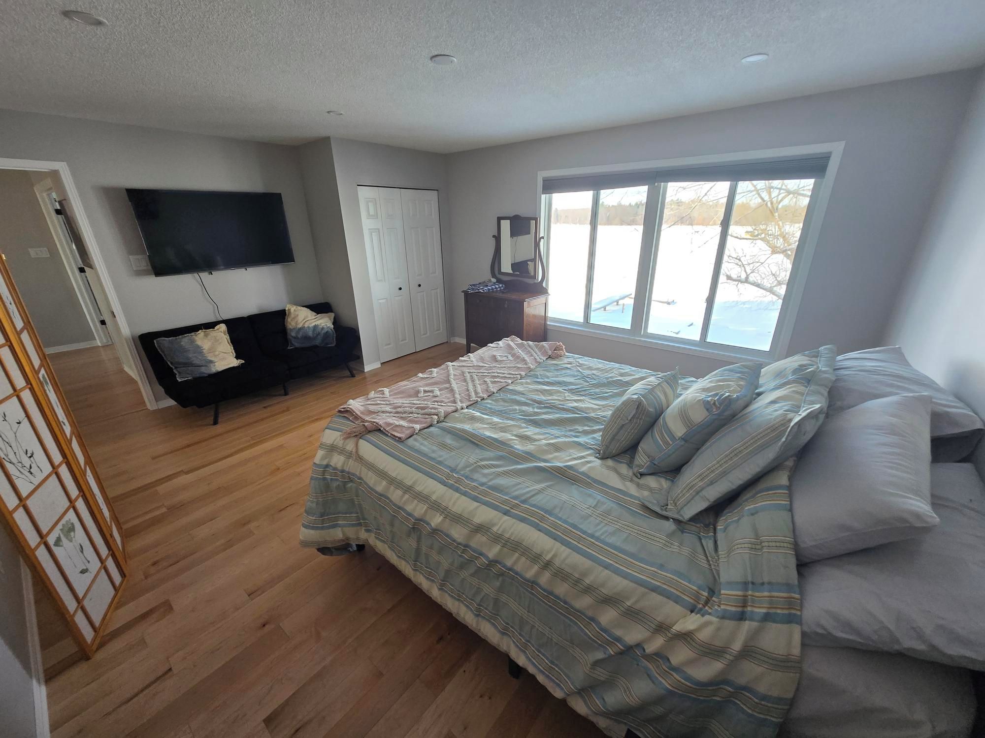 A bedroom with a large bed, a TV, a dresser, and a window with a view.
