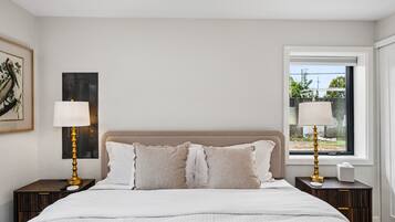 A bedroom with a bed, two bedside tables, a window, and a wall-mounted lamp.