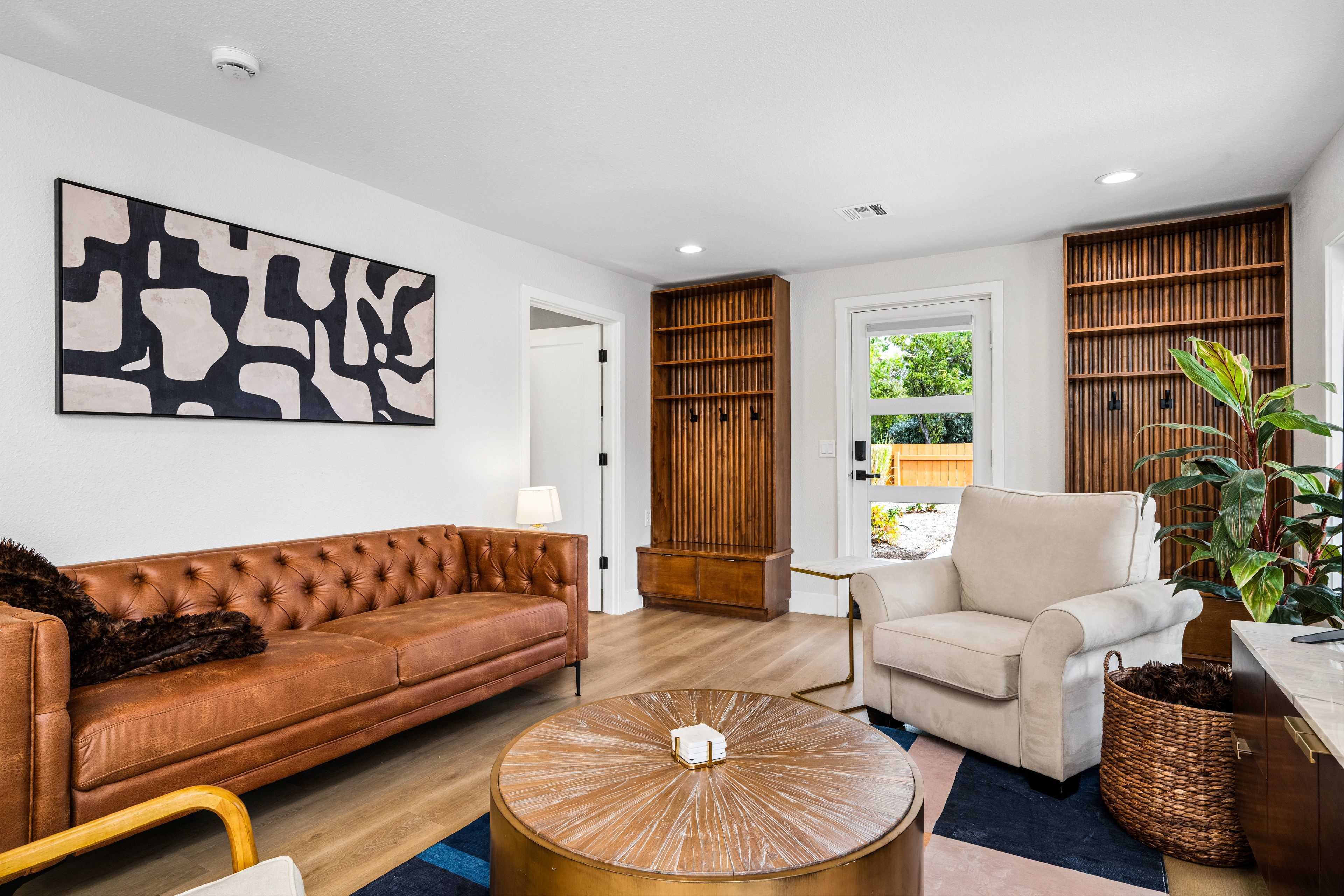 Een moderne woonkamer met een bruine leren bank, een witte fauteuil, een ronde salontafel en een groot abstract schilderij aan de muur.