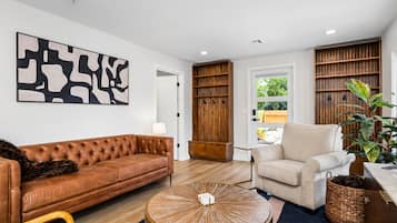 Een moderne woonkamer met een bruine leren bank, een witte fauteuil, een ronde salontafel en een groot abstract schilderij aan de muur.