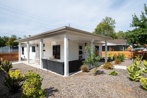 A single-story house with a covered porch, a small garden with various plants, and a wooden fence in the background. - South Campus Modern - Upscale & Walkable to UO, Park & Shops (Eugene)