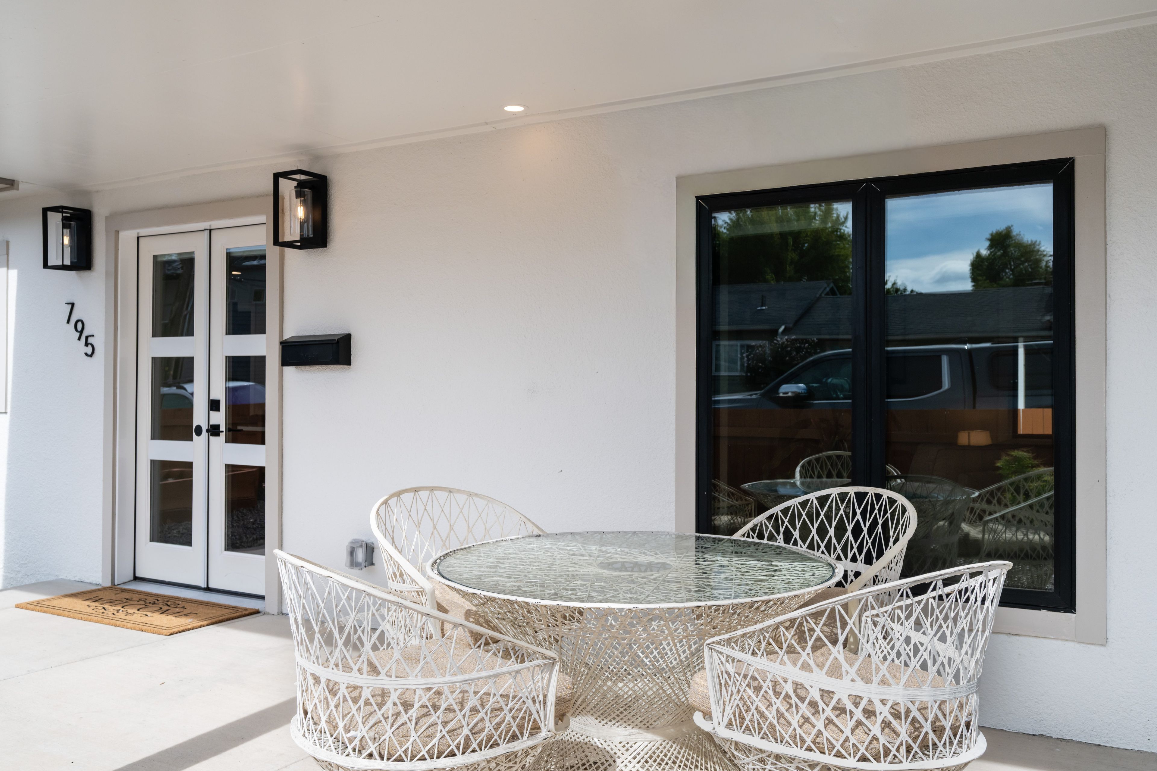 A patio with a round table and four wicker chairs, a door with glass panels, and a mailbox on the wall.