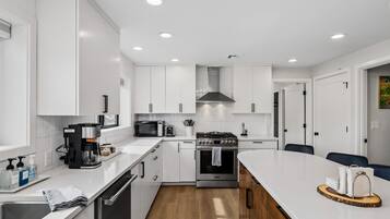 A modern kitchen with white cabinetry, a stainless steel stove, a microwave, and a coffee maker.