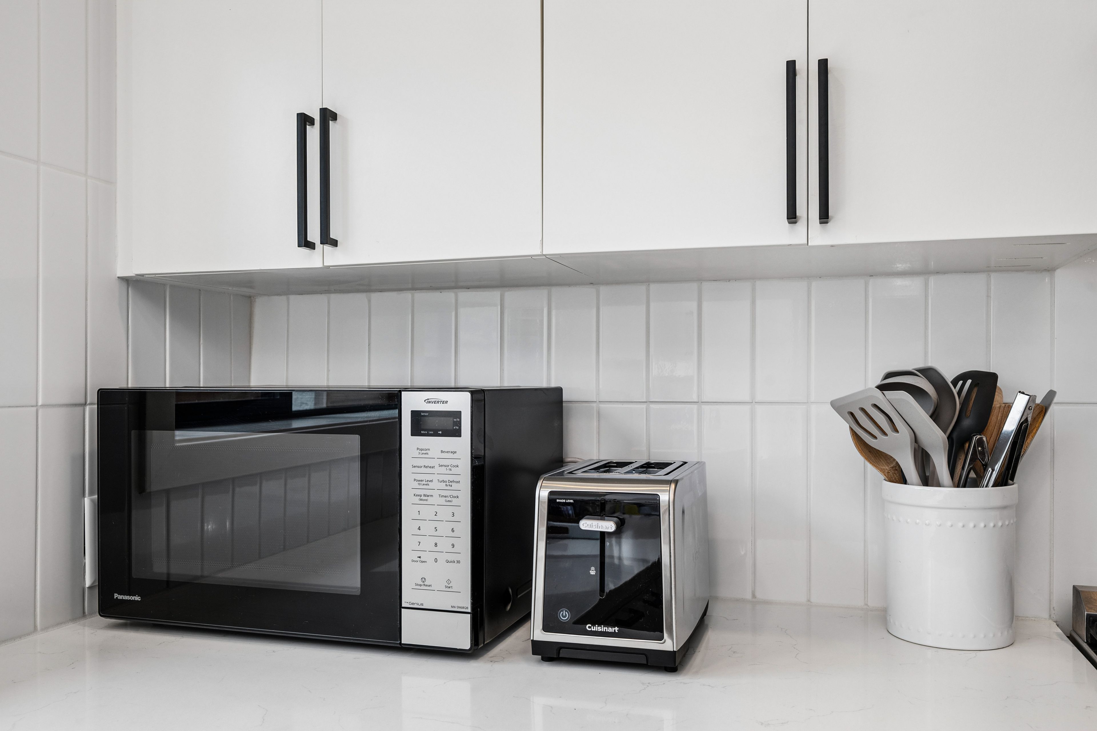 A kitchen with white cabinets, a microwave, a toaster, and a utensil holder.