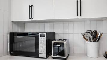 A kitchen with white cabinets, a microwave, a toaster, and a utensil holder.