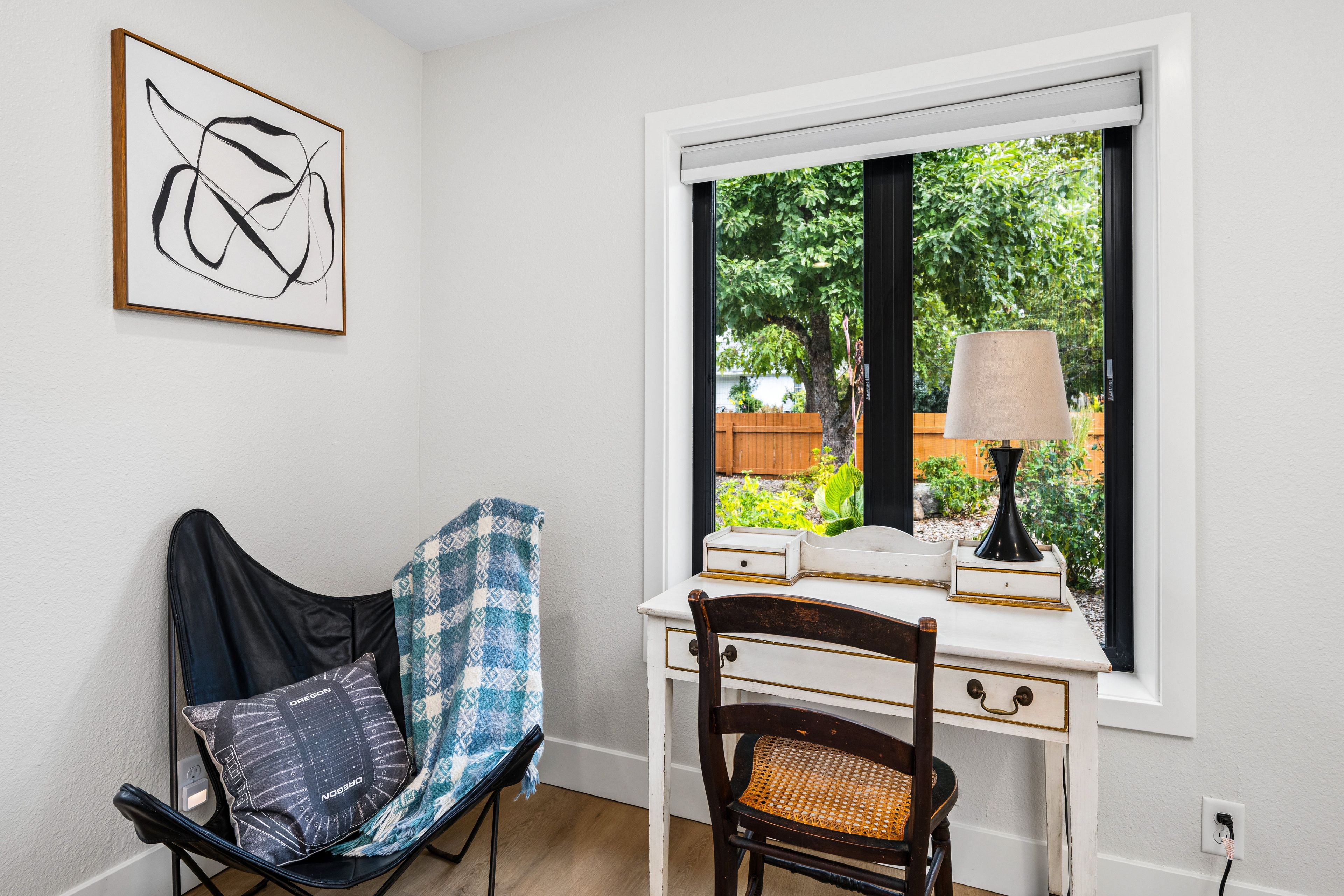 Quarto com escrivaninha, cadeira e janela com vista para área verde.